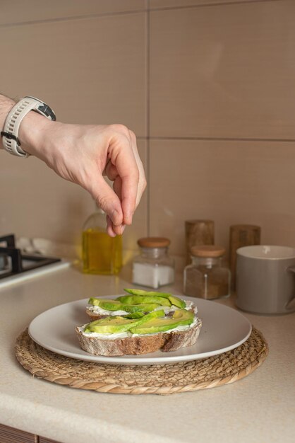 Junger Mann bereitet Toast mit Avocado und Ei zum Frühstück in der Küche zu