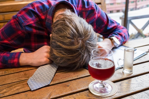 Junger Mann, der Alkohol trinkt, liegt oder schläft auf dem Tisch in der Bar