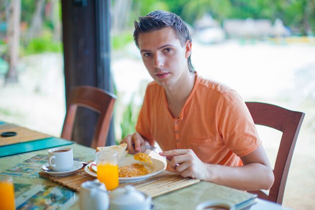 Junger Mann, der am Erholungsortrestaurant frühstückt