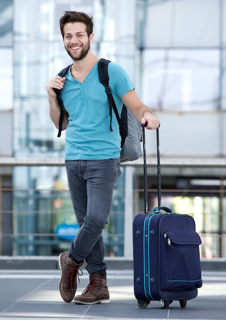 Junger Mann, der am Flughafen mit Koffer und Tasche wartet