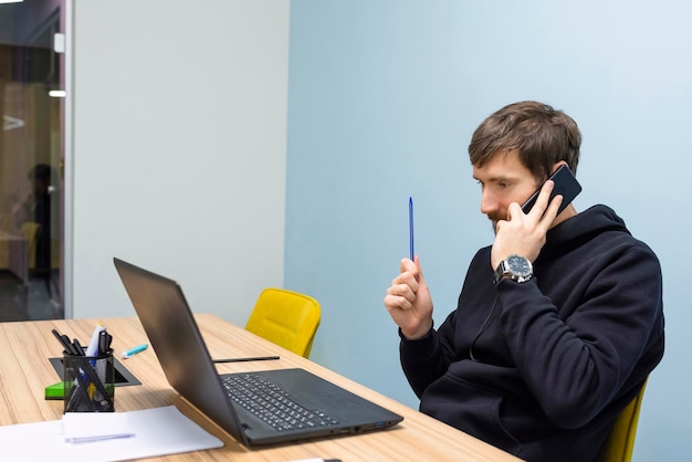 Junger Mann, der am Schreibtisch im Büro arbeitet und am Telefon spricht Geschäftskonzept