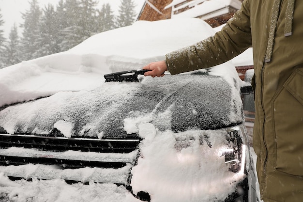 Junger Mann, der am Wintertag in der Nähe Schnee vom Auto im Freien putzt