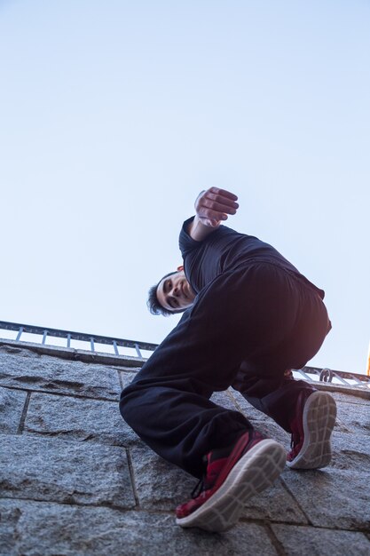 Junger mann, der an der wand hängt und versucht, beim handeln von parkour oben zu klettern.