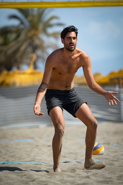 Foto junger mann, der an einem sonnigen tag beachvolleyball am strand spielt