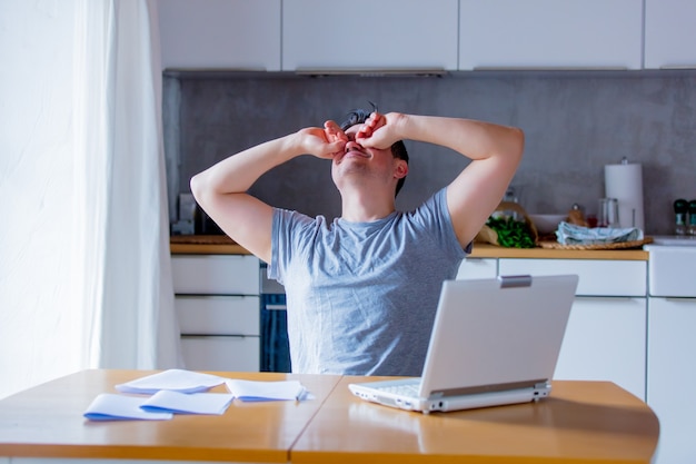 Junger Mann, der Arbeit im Internet beim Sitzen an der Küche mit Laptop-Computer sucht.