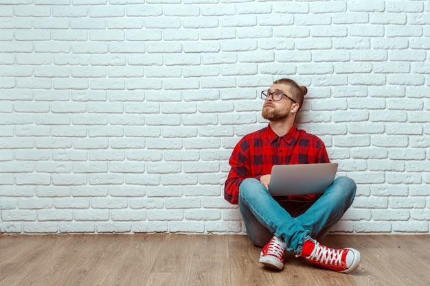 Junger Mann, der auf Boden mit Laptop sitzt