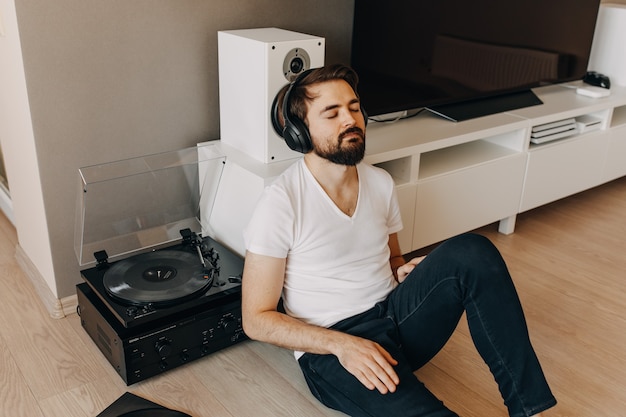 Junger Mann, der auf dem Boden sitzt und Musik auf einem Vinyl-Spieler hört