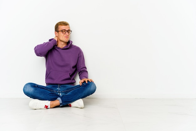 Junger Mann, der auf dem Boden sitzt und Nackenschmerzen aufgrund des sitzenden Lebensstils leidet