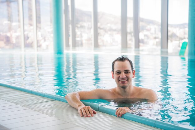 Junger Mann, der auf einem Luxusdachpool schwimmt und an der Kamera im Fünf-Sterne-Hotel-Spa lächelt