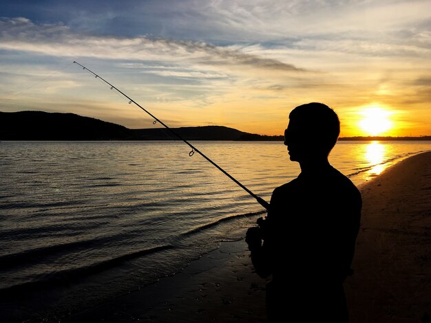 Junger Mann, der auf einem See bei Sonnenuntergang fischt