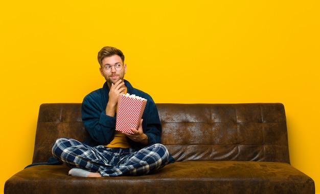 Junger Mann, der auf einem Sofa mit Popcorn sitzt. Kino-Konzept