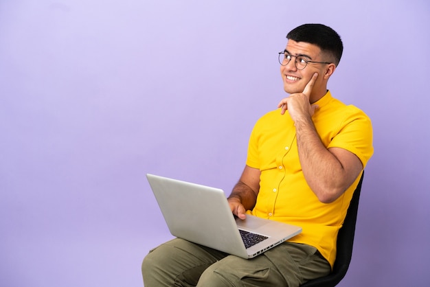 Junger Mann, der auf einem Stuhl mit Laptop sitzt und eine Idee denkt, während er nach oben schaut