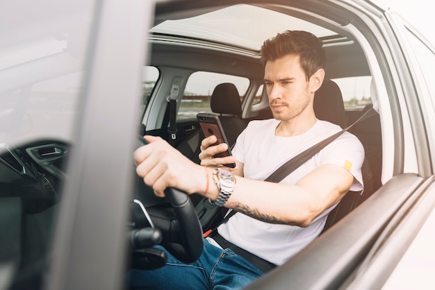 Junger Mann, der Auto unter Verwendung des Smartphone fährt