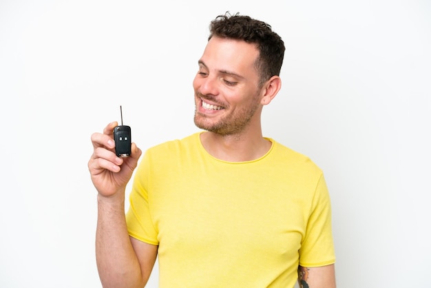 Junger Mann, der Autoschlüssel lokalisiert auf weißem Hintergrund mit glücklichem Ausdruck hält