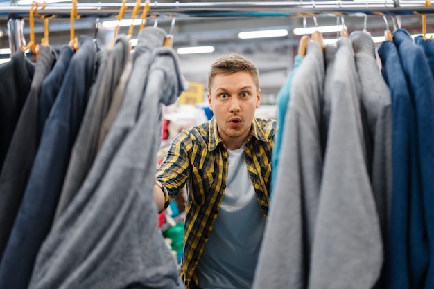 Junger Mann, der Bademantel im Bettwäschespeicher wählt. Männliche Person, die Haushaltswaren im Markt kauft, Kerl im Bettwarengeschäft