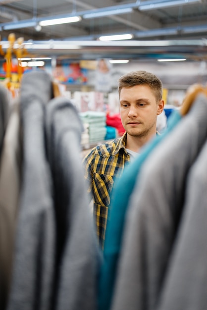 Junger Mann, der Bademantel im Bettwäschespeicher wählt