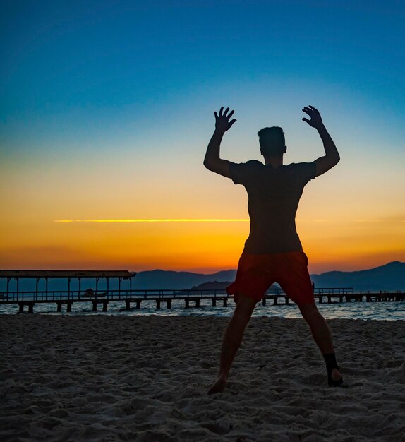 Junger Mann, der bei vollem Sommersonnenuntergang am Strand von Florianopolis, Brasilien, körperliche Übungen macht