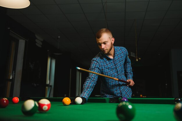 Junger Mann, der Billard im dunklen Billardclub spielt