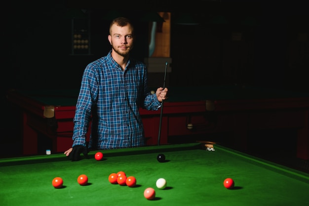 Junger Mann, der Billard im dunklen Billardclub spielt