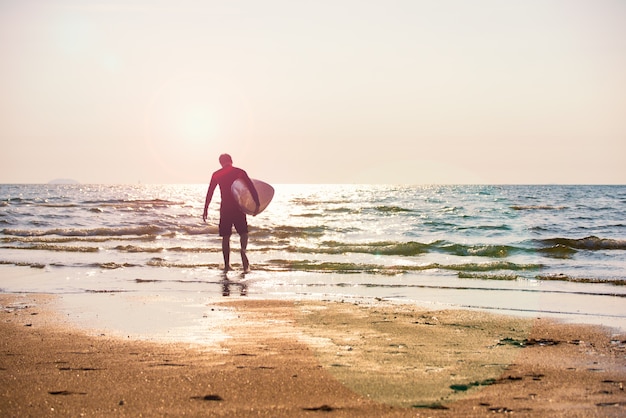 Foto junger mann, der das surfbrett läuft auf die küste hält