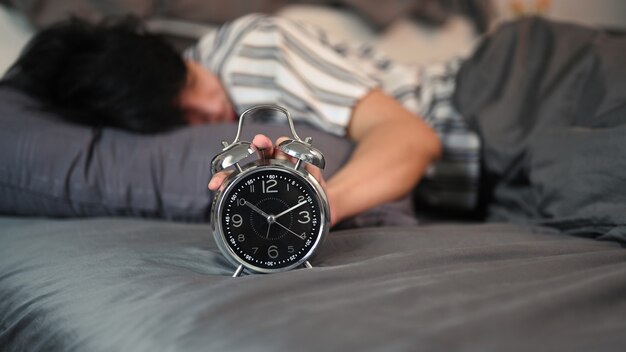 Junger Mann, der den Wecker auf seinem Bett stoppt.