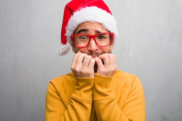 Junger Mann, der den Weihnachtstag hält Geschenke beißend Nägeln, nervös und sehr besorgt feiert