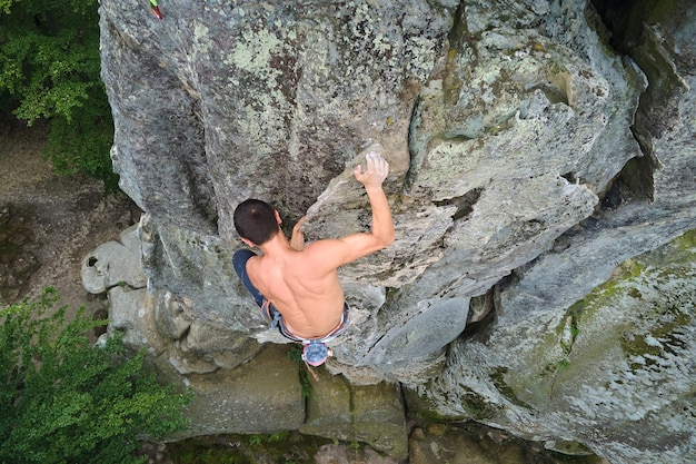 Junger Mann, der die steile Wand des felsigen Berges erklimmt Männlicher Kletterer überwindet die anspruchsvolle Route Engagement im Extremsportkonzept