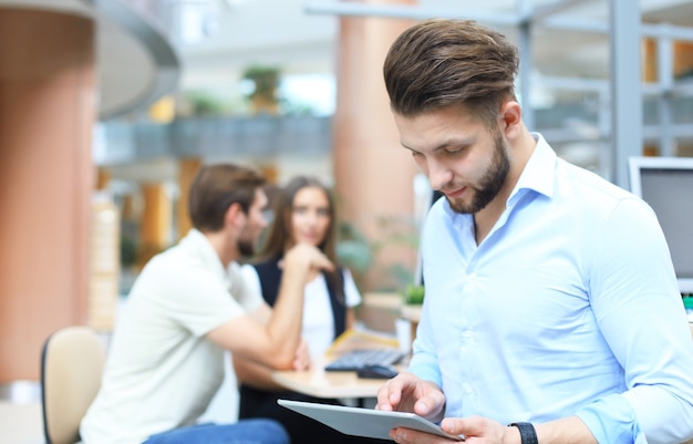 Junger Mann, der digitales Tablet hält, während seine Kollegen im Hintergrund arbeiten.