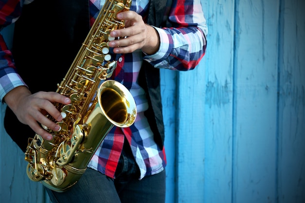 Junger Mann, der draußen auf Saxophon nahe der alten Mauer spielt