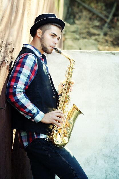 Junger Mann, der draußen auf Saxophon nahe der alten Mauer spielt