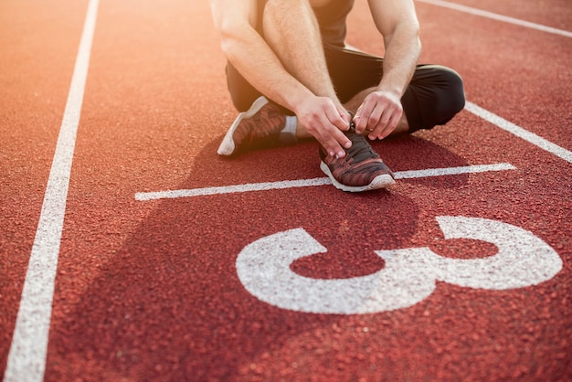 Junger Mann der Eignung, der auf Anfangslinie über dem roten Leichtathletikfeld sitzt