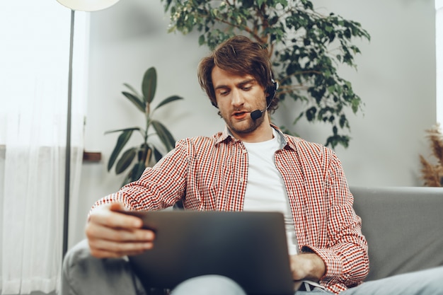 Junger Mann, der ein Headset trägt, das einen Videoanruf durch Laptop tut