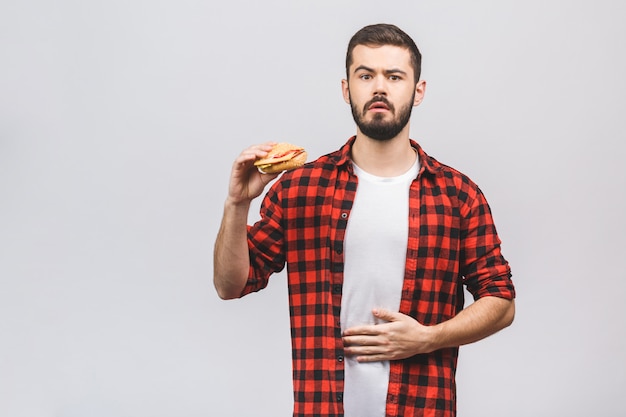 Junger Mann, der ein Stück Hamburger hält. Diätkonzept isoliert gegen weißen Hintergrund.