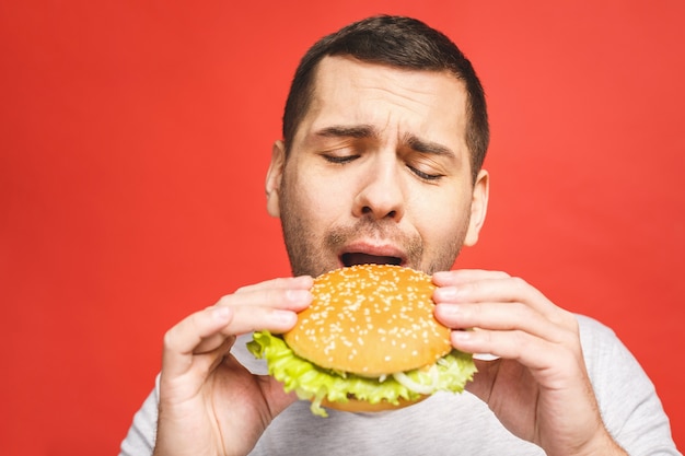 Junger Mann, der ein Stück Hamburger hält