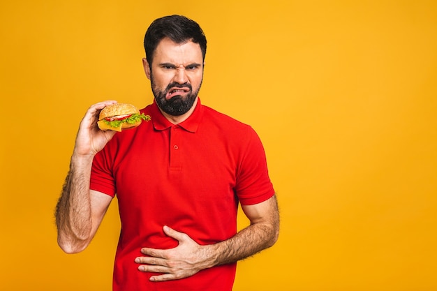 Junger Mann, der ein Stück Sandwich hält. Student isst Fast Food. Burger ist kein hilfreiches Essen.