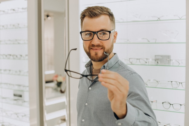 Junger Mann, der eine Brille im Optikgeschäft wählt