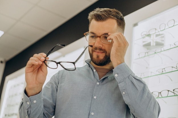 Junger Mann, der eine Brille im Optikgeschäft wählt