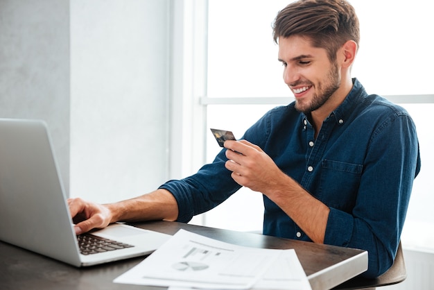 Junger Mann, der eine Kreditkarte hält und tippt. Online-Shopping im Internet mit einem Laptop. Blick auf den Laptop