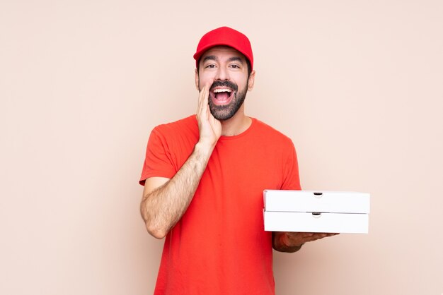 Junger Mann, der eine Pizza über lokalisiertem etwas schreien und ankündigen hält