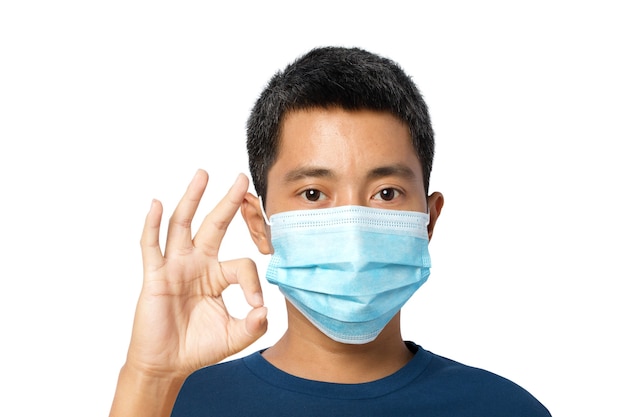 Junger Mann, der eine schützende Gesichtsmaske trägt, zeigt das OK-Zeichen isoliert auf weißem Hintergrund. Beschneidungspfad.