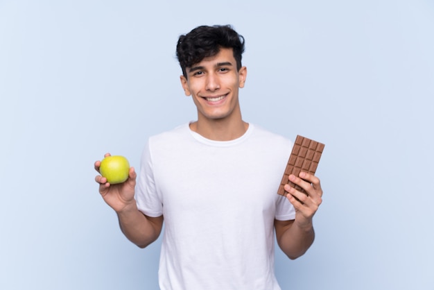 Junger Mann, der einen Apfel und eine Schokolade über lokalisierter Wand hält