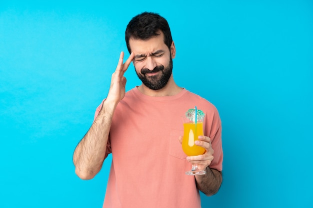 Junger Mann, der einen Cocktail über Blau mit Kopfschmerzen hält