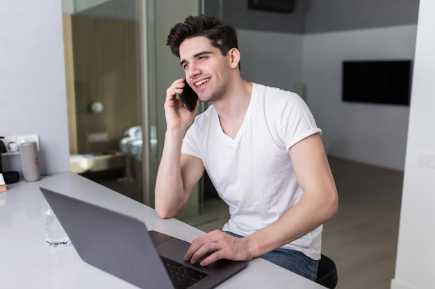 Junger Mann, der einen Laptop am Telefon zu Hause benutzt