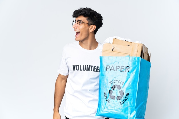 Junger Mann, der einen Recyclingbeutel voll Papier hält, der in seitlicher Position lacht