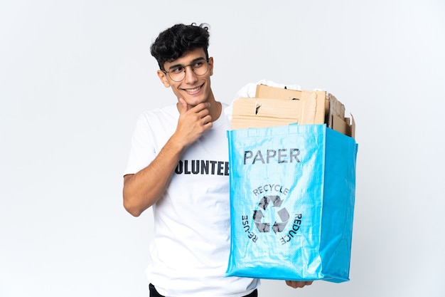 Junger Mann, der einen Recyclingbeutel voll Papier hält, der zur Seite schaut und lächelt