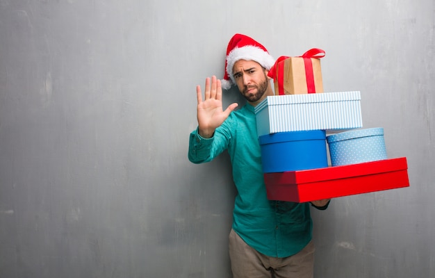 Junger Mann, der einen Sankt-Hut hält die Geschenke hält Hand in Front trägt