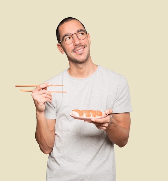 Junger Mann, der Essstäbchen verwendet, um Sushi zu essen