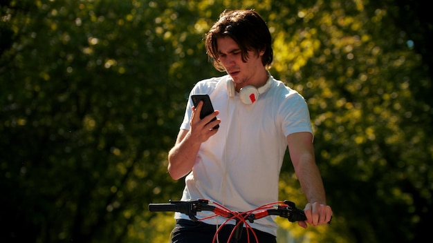 Junger Mann, der Fahrrad fährt und auf sein Telefon schaut