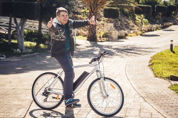 Junger Mann, der Fahrrad im Park reitet, der sich Daumen zeigt.