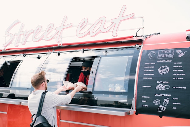 Junger Mann, der Fastfood einnimmt, der von einem LKW-Angestellten gehalten wird?